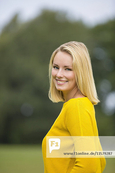 Porträt einer hübschen blonden Frau im Park  die vor der Kamera lächelt.