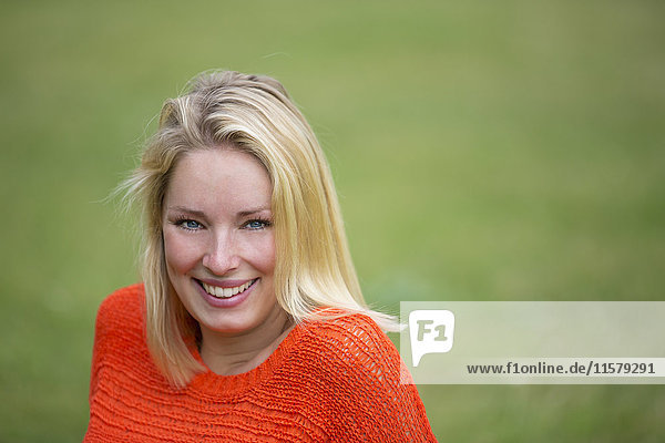 Portrait of a blonde woman sitting in the park and smiling at camera