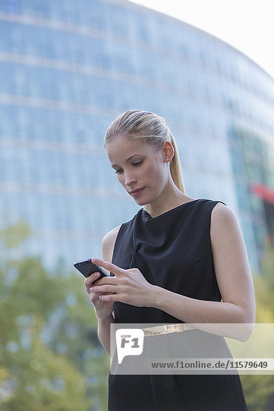 Hübsche elegante Frau mit Handy vor einem Bürogebäude