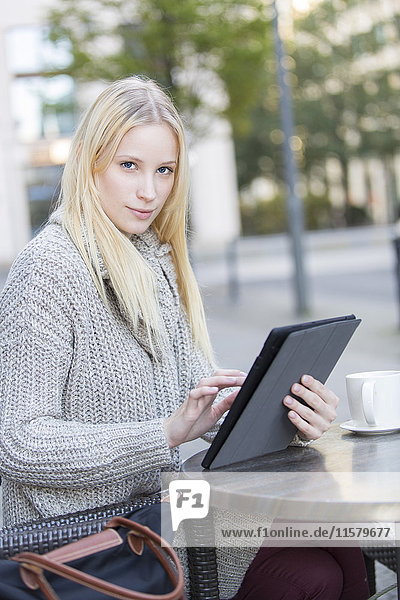 Hübsche junge Frau mit Tablette in einem Cafe im Stadtzentrum mit Blick auf die Kamera