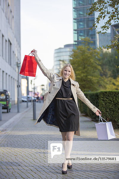 Hübsche blonde Frau mit erhobenen Armen und Einkaufstaschen in der Innenstadt.