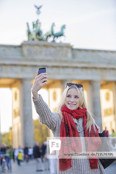 Hübsche blonde Frau mit einem Selfie vor dem Brandenburger Tor in Berlin.