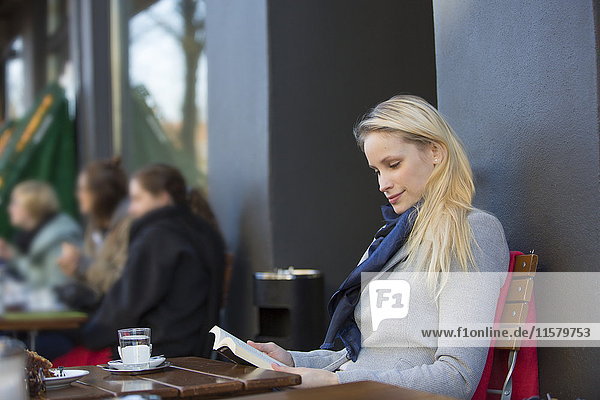 Hübsche blonde Frau liest ein Buch in einem Cafe in der Innenstadt.