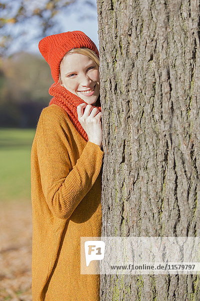 Hübsche blonde Frau  die sich im Herbst im Park an einen Baum lehnt.