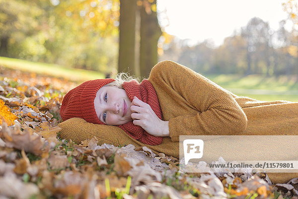Hübsche blonde Frau im Park im Herbst lächelnd vor der Kamera liegend