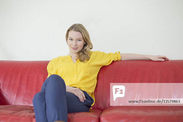 Porträt einer hübschen blonden Frau auf der Couch mit Blick auf die Kamera