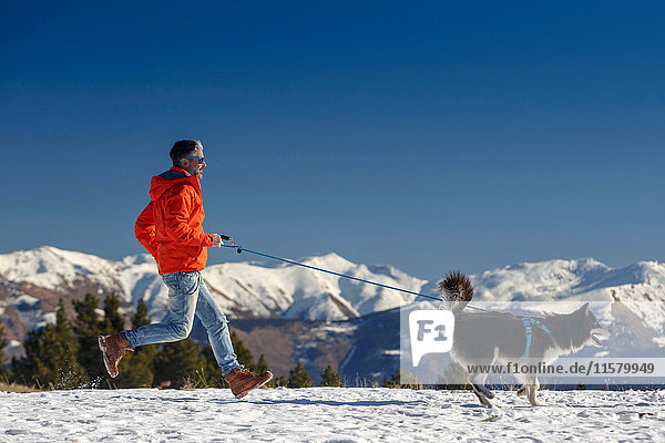 Mann rennt mit Hund in schneebedeckter Berglandschaft