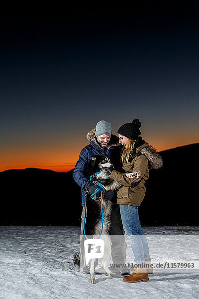 Paar spielt nachts mit Hund im Schnee