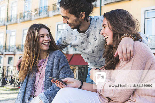 Drei Freunde im Freien lachend junge Frau mit Smartphone in der Hand Lissabon Portugal