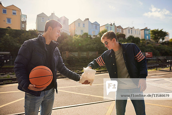 Junger Mann teilt eine Tüte Chips mit einem Freund  junger Mann hält Basketball  Bristol  UK