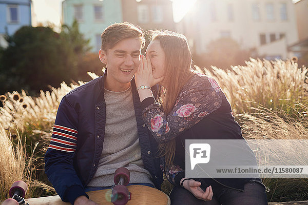 Two friends sitting outdoors  young woman whispering to young man  Bristol  UK