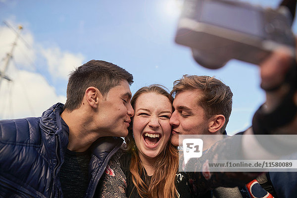 Drei Freunde beim Selbstauslöschen mit der Kamera  junge Männer küssen junge Frau auf die Wange  Bristol  UK