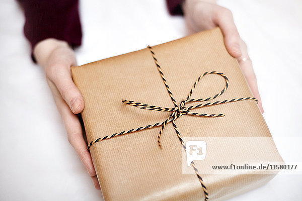 Frau hält in braunem Papier verpacktes Geschenk  mit Schnur verziert  Nahaufnahme