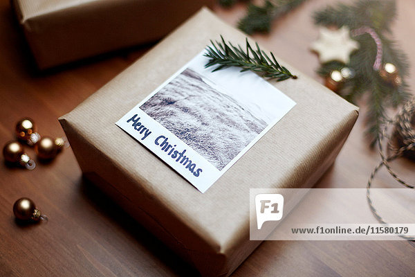 Geschenk in braunes Papier eingewickelt und mit Farn und Notizzetteln verziert: Frohe Weihnachten