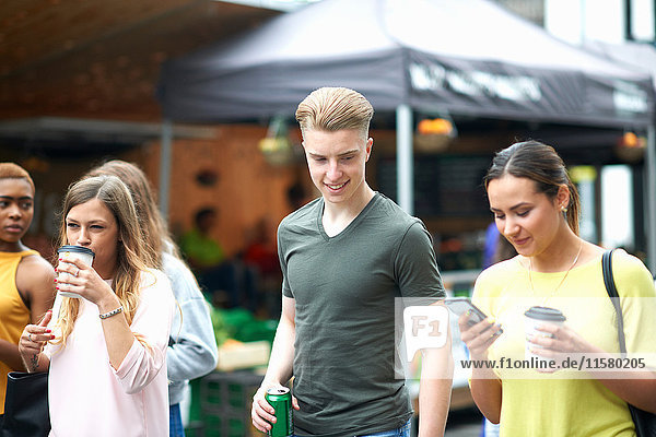 Gruppe von Freunden  Spaziergang im Freien  Getränke tragen  Smartphone anschauen