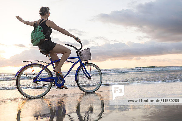 Frau winkt beim Radfahren am Strand bei Sonnenuntergang  Nosara  Provinz Guanacaste  Costa Rica