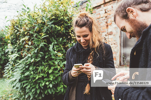 Ehepaar im Garten beim Betrachten von Smartphones