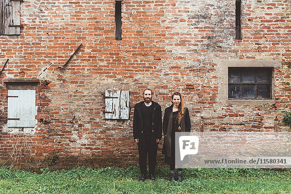 Porträt eines Ehepaares vor einem alten Bauernhaus mit Backsteinmauer
