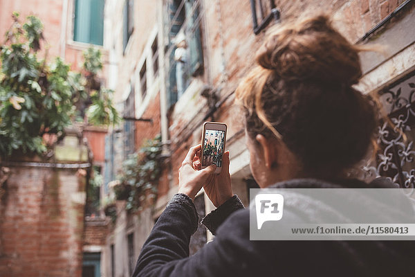 Über-die-Schulter-Ansicht einer Frau  die Gebäude mit einem Smartphone fotografiert  Venedig  Italien