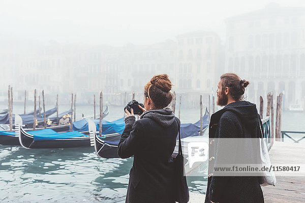 Couple photographing gondolas on misty canal  Venice  Italy