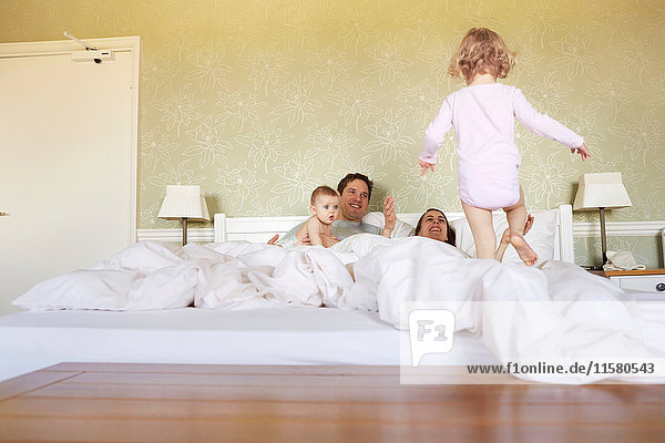 Female toddler stepping on bed with parents and baby sister