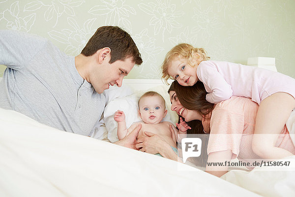 Female toddler and baby sister playing in bed with parents