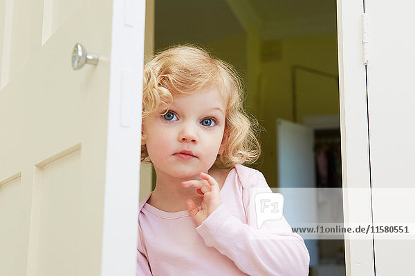 Female toddler peering from door