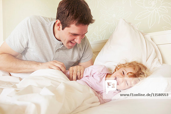 Mittelgroßer Erwachsener Mann kitzelt Kleinkind Tochter im Bett
