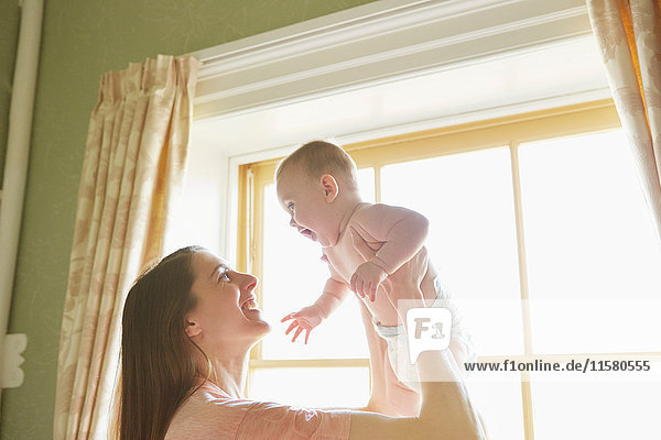 Mid adult woman holding up baby daughter in bedroom