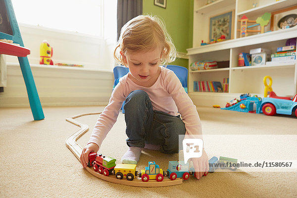Female toddler playing with toy train on playroom floor