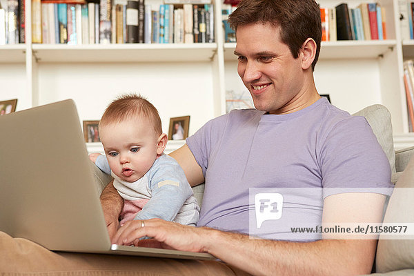 Kleines Mädchen hilft Vater mit Laptop beim Tippen auf dem Sofa