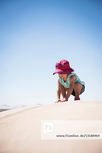 Female toddler crouching on top of sand dune  Little Sahara  Utah  USA