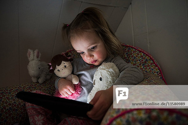 Weibliches Kleinkind sitzt im Bett und starrt auf ein digitales Tablett