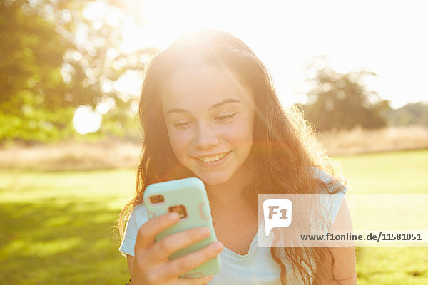 Mädchen schaut auf Smartphone im sonnenbeschienenen Park