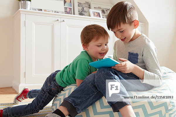 Male toddler and brother on beanbag chair looking at digital tablet
