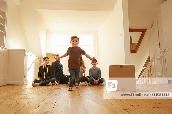 Porträt eines männlichen Kleinkindes und einer Familie  die auf dem Boden in einem neuen Zuhause sitzen.