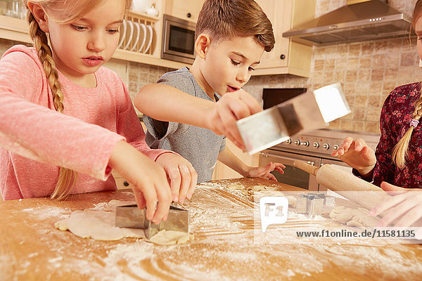 Girls and boy baking star shape pastry at kitchen table