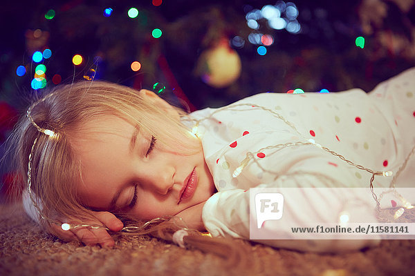 Girl wearing lights asleep on floor at christmas