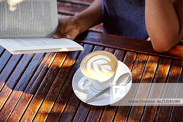 Junge Frau sitzt im Freien  liest ein Buch  Kaffee vor sich  Mittelteil