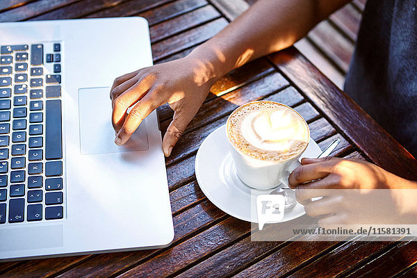 Junge Frau sitzt im Freien  benutzt Laptop  trinkt Kaffee  Mittelteil