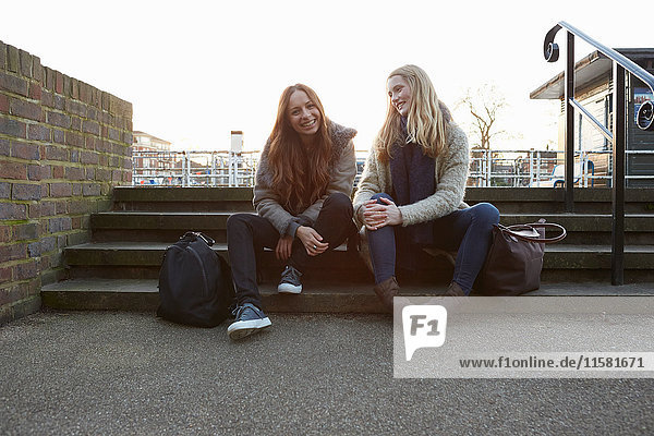 Zwei Freundinnen im Freien  auf einer Treppe sitzend  lächelnd