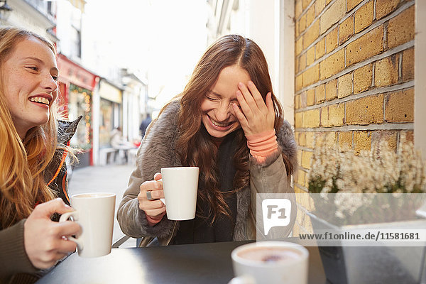 Zwei Freundinnen  die im Freien sitzen  Kaffee trinken  lachen