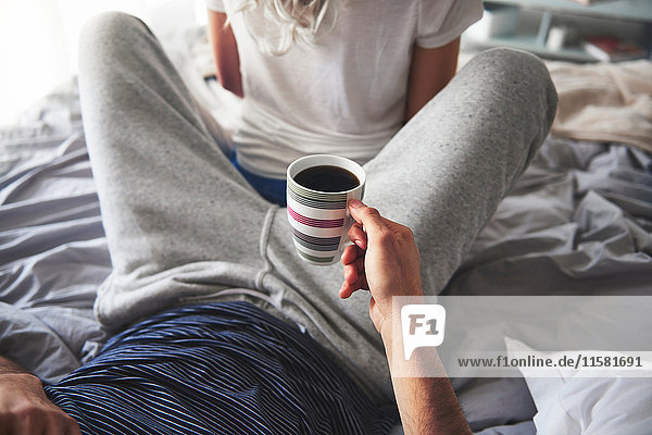 Mann entspannt sich auf dem Bett  hält eine Tasse Kaffee  Frau sitzt mit dem Rücken zu ihm