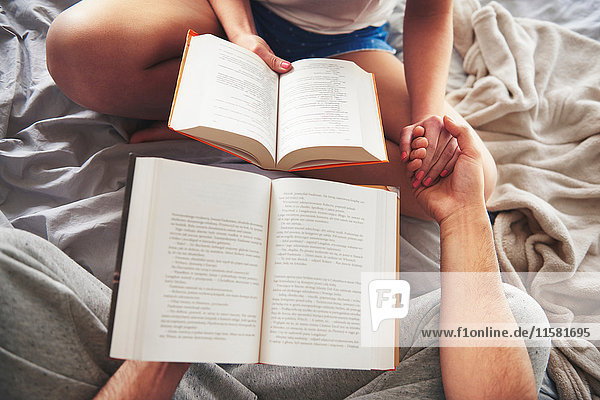 Couple sitting on bed  holding books  holding hands  low section