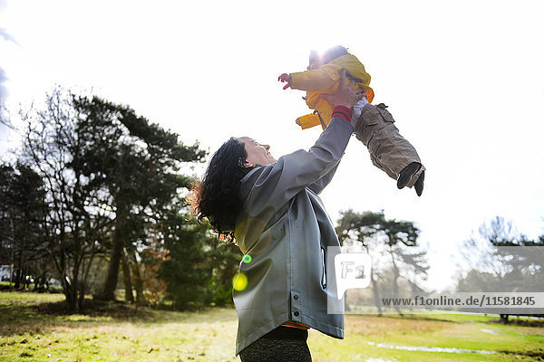 Reife Frau  die sich hochhält und mit ihrem kleinen Sohn im Park spielt