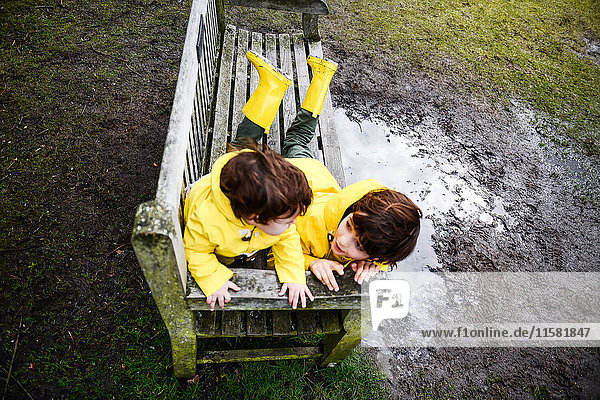 Draufsicht auf den kleinen Jungen und Bruder in gelben Anoraks auf der Parkbank