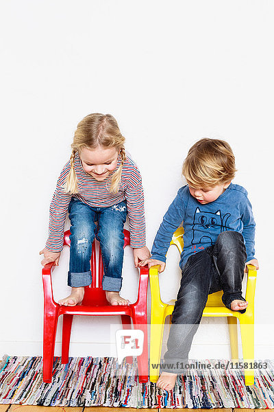 Young boy and girl   crouching on colourful chairs