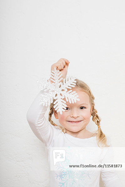 Porträt eines jungen Mädchens vor weißem Hintergrund  das eine Schneeflocke hält