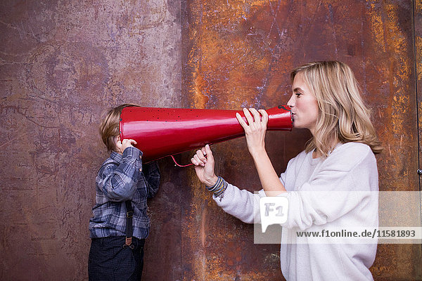 Woman speaking into megaphone  young boy listening  head in megaphone