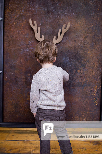 Young boy standing facing wall  cardboard reindeer cut out on wall behind him